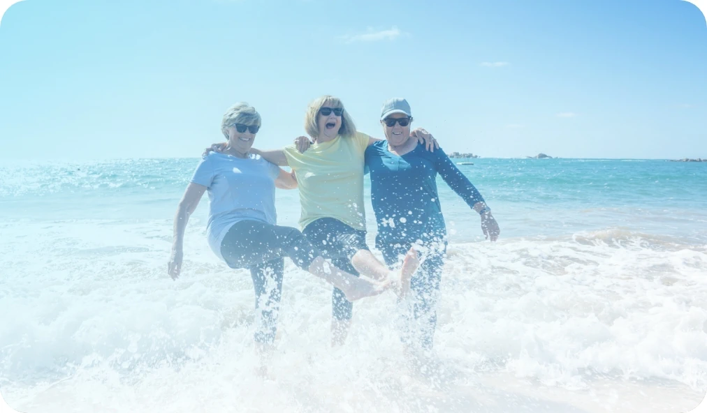 Three happy senior women standing in the ocean, kicking water towards the camera.